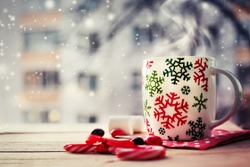 Hot Coffee cup on a frosty winter day window background with candy canes /Christmas holidays background/ Winter cozy background 