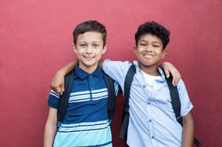 Best children friends standing with hand on shoulder against red background. Happy smiling classmates standing together on red wall. Portrait of multiethnic schoolboys enjoying friendship.