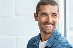 Confident young man looking away with big smile. Happy handsome guy looking through window thinking about the future. Closeup face of smiling casual man imagine with copy space.