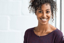 Portrait of a beautiful african woman smiling. Young black woman in casual looking at camera with copy space. Portrait of cheerful girl with afro hair sitting near a window.