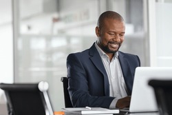Positive mature businessman working on laptop in modern office. Successful african business man working on computer while sitting at desk. Smiling middle aged man working in a corporate.