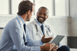 Two mature smiling doctors having discussion about patient diagnosis, holding digital tablet. Representative pharmaceutical discussing case after positive result with happy doctor about new medicine.