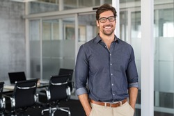 Portrait of young businessman wearing eyeglasses and standing outside conference room. Portrait of happy business man wearing spectacles and looking at camera with copy space. Satisfied proud man.