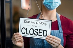 Businesswoman closing her business activity due to covid-19 lockdown. Owner with surgical mask close the doors of her store due to quarantine coronavirus. Close up sign due to the effect of COVID-19.