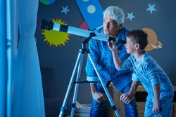 Grandfather teaching grandson using telescope to see the constellations and moon. Child seeing satellite using telescope with senior man. Granddad and grandchild using telescope to see moon surface.