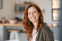 Portrait of smiling mature woman looking at camera with big grin. Successful middle aged woman at home smiling. Beautiful mid adult lady with long red hair enjoying whitening teeth treatment.