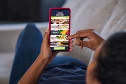 Woman lying on couch using food delivery app on smartphone. Close up of african woman hands holding cellphone and ordering food online.