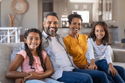 Portrait of cheerful ethnic family at home sitting on sofa and looking at camera. Happy indian family with two children relaxing at home. Mixed race parents with their daughters in new home.