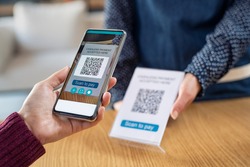 Close up of woman hand holding smartphone and scanning qr code for digital payment. Customer paying money online using mobile phone after shopping. Girl using cellphone scanner to scan qr code.
