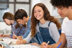 Satisfied young woman looking at camera. Team of multiethnic students preparing for university exam. Portrait of girl with freckles sitting in a row with her classmates during high school exam.
