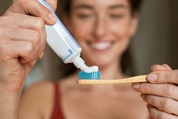 Close up of woman with tooth brush applying paste in bathroom. Closeup of girl hands squeezing toothpaste on ecological wooden brush. Smiling woman applying toothpaste on eco friendly toothbrush.