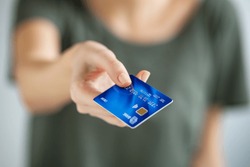 Close up of young woman hand holding credit card. Woman extending hand to give credit card to cashier. Close up of a girl paying with blue creditcard.