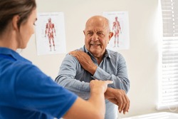 Physiotherapist helping senior man with elbow exercise in clinic. Doctor checking elbow of senior patient. Old man during an appointment with professional osteopath working and massaging his shoulder.