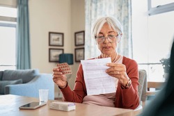 Senior woman checking prescription and dosage of medicine. Elderly lady reading medical instructions before taking medicine. Senior woman reading side effects list of drug and contraindications.