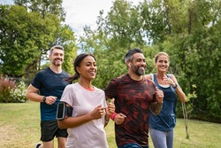 Healthy group of multiethnic middle aged men and women jogging at park. Happy mixed race couples running together. Mature friends running together outdoor.