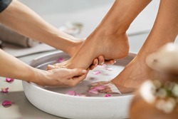Close up of hands of masseur washing feet of woman in spa in grey bowl with water. Girl getting spa massage treatment in luxury beauty salon: foot reflexology and chiropody therapy.