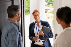 Smiling mature social counselor meeting mature couple at home. Happy multiethnic man and latin woman greeting agent at home standing near door. Successful social worker consultant on the doorstep.