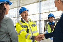 Smiling civil engineer shaking hands at construction site with businesswoman. Construction manager and supervisor shaking hand on building site. Team of workers conclude an agreement with an handshake