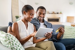 Black wife doing shopping online while using digital tablet at home with husband. Couple using bank card to pay bills or to book their next vacation. Mature couple making an online purchase.