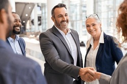 Happy mature businessman shaking hands with businesswoman in modern office. Successful entrepreneur greeting business woman with handshake. Agreement and business deal concept.