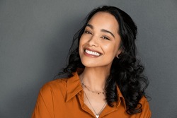 Close up face of young woman with beautiful smile isolated on grey wall with copy space. Successful multiethnic girl. Latin woman looking at camera against gray wall with a big whitening teeth smile.