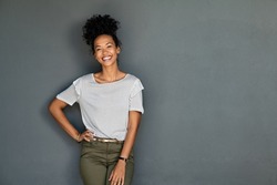 Portrait of young african american woman standing with hands on waist and looking at camera. Confident stylish black girl standing against grey background. Happy afro girl smiling with copy space.