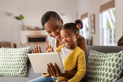 Smiling ethnic mother and funny daughter on video call using digital tablet at home. African american mature mother and little girl using digital tablet while making video call and waving hello.