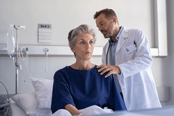 Physician listening senior woman back lungs through stethoscope. Hospitalized elderly woman sitting on bed while doctor checking her breathe and heartbeat. Doctor auscultate heart of old patient.
