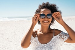 Portrait of smiling african american woman wearing sunglasses at the beach with copy space. Happy black girl wearing fashionable specs while smiling at seaside. Beautiful woman relaxing at sea.