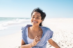 Smiling young latin woman running on beach with a big grin. Mixed race girl enjoying vacation while running on beach. Carefree hispanic woman having fun at sea in summer.