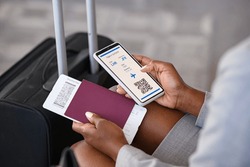 Close up hand of black businesswoman checking flight eticket on phone while holding passport and boarding pass. African american woman hand checking online travel plane ticket on mobile phone.