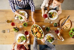Top view of man passing food bowl to friend. High angle view of happy young friends eating together at home. Happy men and women having lunch with roasted chicken.