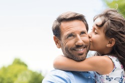 Portrait of a little girl kissing her dad on cheek. Pretty girl giving a kiss to her father outdoor. Loving child embrace and kissing her father.