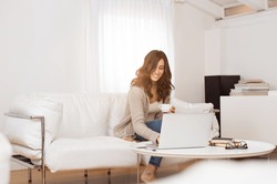 Young beautiful woman holding coffee mug and typing on laptop. Pretty girl sitting on a sofa using laptop at home in the living room.Woman drinking a cup of tea while surfing the net with computer.