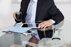 Midsection of young businessman with coffee cup using digital tablet at desk in office
