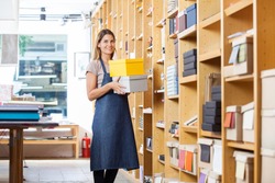 Portrait of confident mid adult woman carrying boxes in store