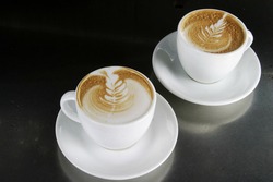Two single cappuccino's sitting ready with latte art