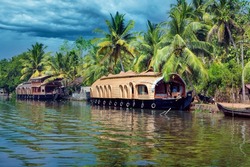 House boat in backwaters near palms at cloudy blue sky in Kumarakam, Kerala, India.