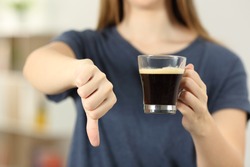 Front view close up of a woman hands holding a coffee cup with thumbs down at home