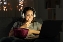 Single woman watching online tv in the night sitting on a couch in the living room at home