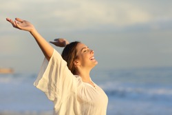 Joyful woman enjoying a day on the beach raising arms at sunset