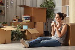 Happy tenant resting drinking coffee moving home sitting on the floor in the night
