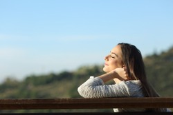 Profile of a relaxed woman sitting on a bench breathing fresh air in the mountain a sunny day