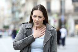 Portrait of a woman in pain holding her chest suffering from lack of breath on a city street