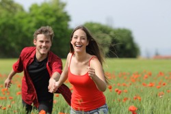 Happy couple running and flirting between the grass on a green poppy field in spring