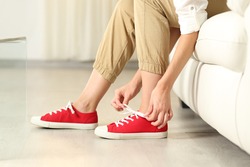 Side view portrait of a woman hands tying shoelaces of sneakers at home