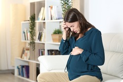 Pregnant woman suffering headache complaining sitting on a sofa in the living room at home