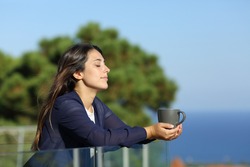 Relaxed woman with closed eyes holding coffee mug in a hotel balcony on the beach