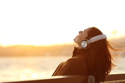 Woman wearing headphones listening to music breathing fresh air relaxing sitting on a bench in winter on the beach