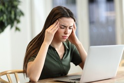 Stressed woman suffering migraine with a laptop sitting in a table at home